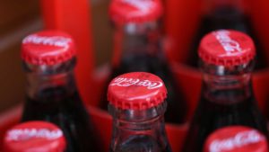 KO stock: Close-up of Coca Cola drink cans lying on paper background