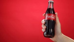 hand holding a bottle of Coca-Cola (KO) against a red background