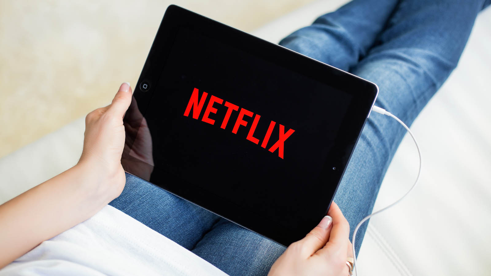NFLX Stock. the netflix logo displayed on a tablet that a person is holding while laying down