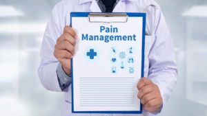 person in white doctor's coat holding a clipboard that says "pain management"