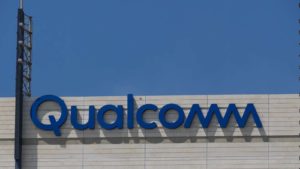 Μια φωτογραφία του λογότυπου της Qualcomm (QCOM) σε ένα γκρίζο κτίριο σε έναν γαλάζιο ουρανό.