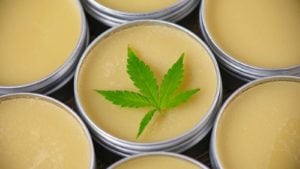 A marijuana leaf rests on top of little tins filled with a balm. 