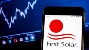 First Solar logo on smartphone in front of computer screen with graphs.  FSLR stock