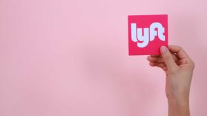 a person holds a pink square with the Lyft logo