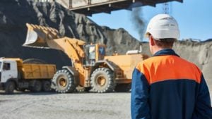 a construction worker looks on as an excavator gets to work in a mine. Mining Stocks