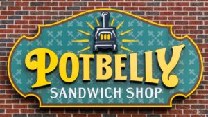 An image of a sign of the green, yellow, black, and brown logo for "Potbelly Sandwich Shop" on a brick wall.