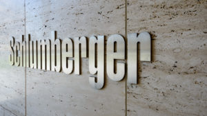 A zoomed in image of the logo for "Schlumberger" reflecting light on a smooth tan stone tiled wall.