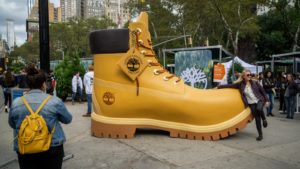A picture of a giant boot on the street surrounded by people.