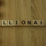An image of letter blocks spelling out "Billionaire" on a wooden surface