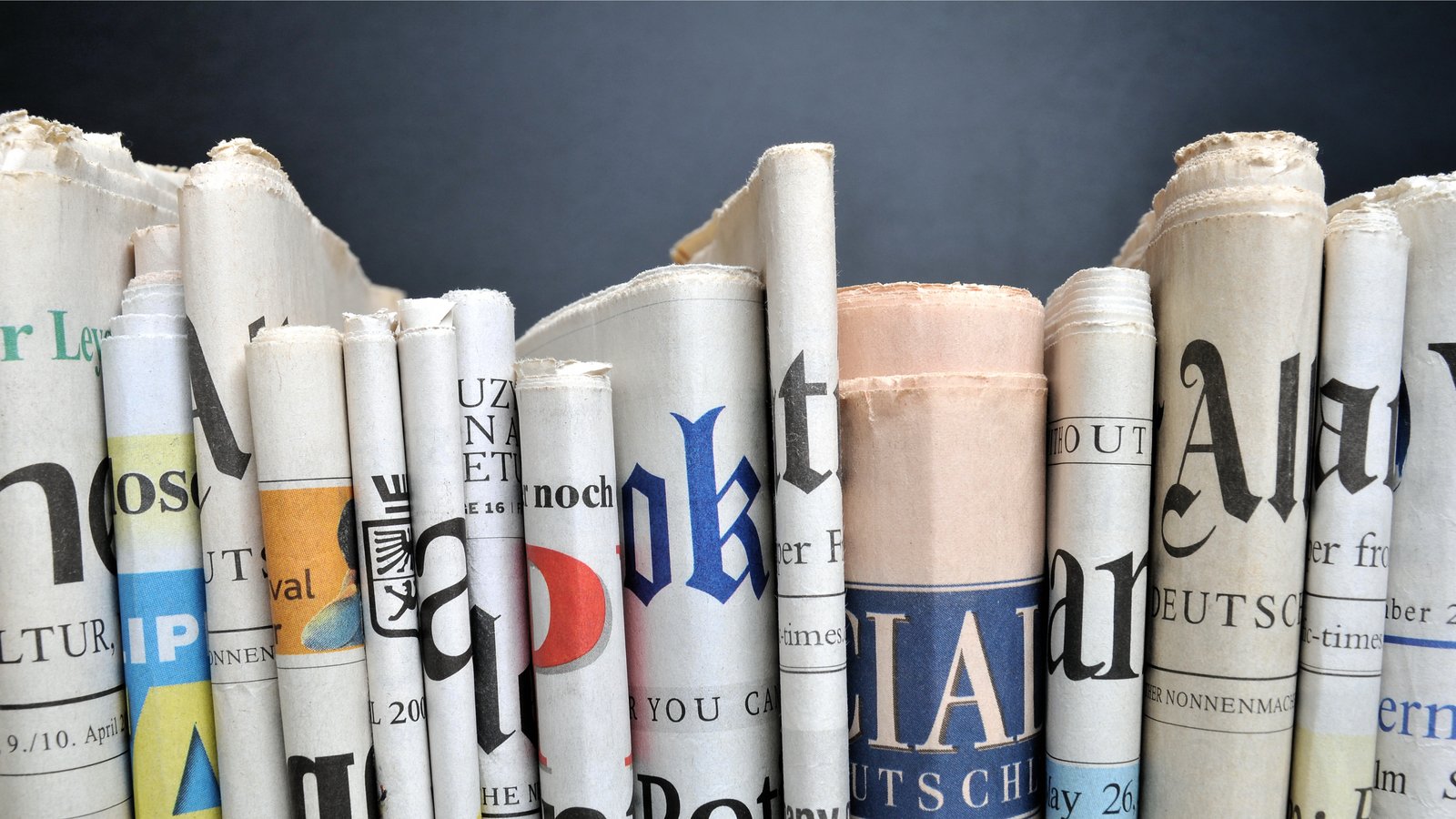 newspapers folded and arranged in row like books on a shelf. gray background.