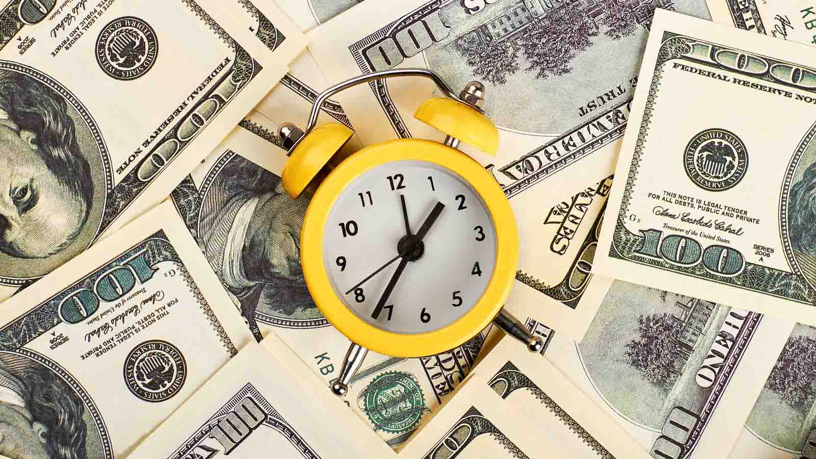 a clock on top of hundred dollar bills to represent short-term stocks
