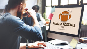 A man looks at a computer monitor with an illustration of a football and "Fantasy Football" in text.
