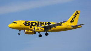 A yellow, Spirit Airlines (SAVE) branded airplane flying in the air representing the Frontier merger.