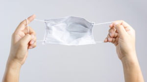 A close-up shot of hands stretching out a disposable face mask.