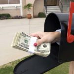 A hand reaches out of a mailbox holding a wad of cash.