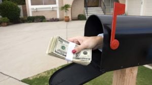 A hand comes out of a mailbox holding a wad of cash.