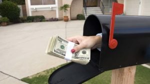 A hand reaches out of a mailbox holding a wad of cash.