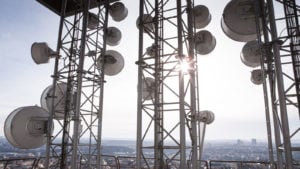 Image of the top of a 5G cell tower with a cityscape and clear blue sky in the background (T-stock)