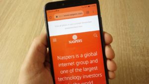a hand holding a phone displaying the Naspers website