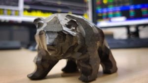An image of a bear figurine in front of blurred computer screens displaying stock charts representing S&P 500 Death Cross 2022.