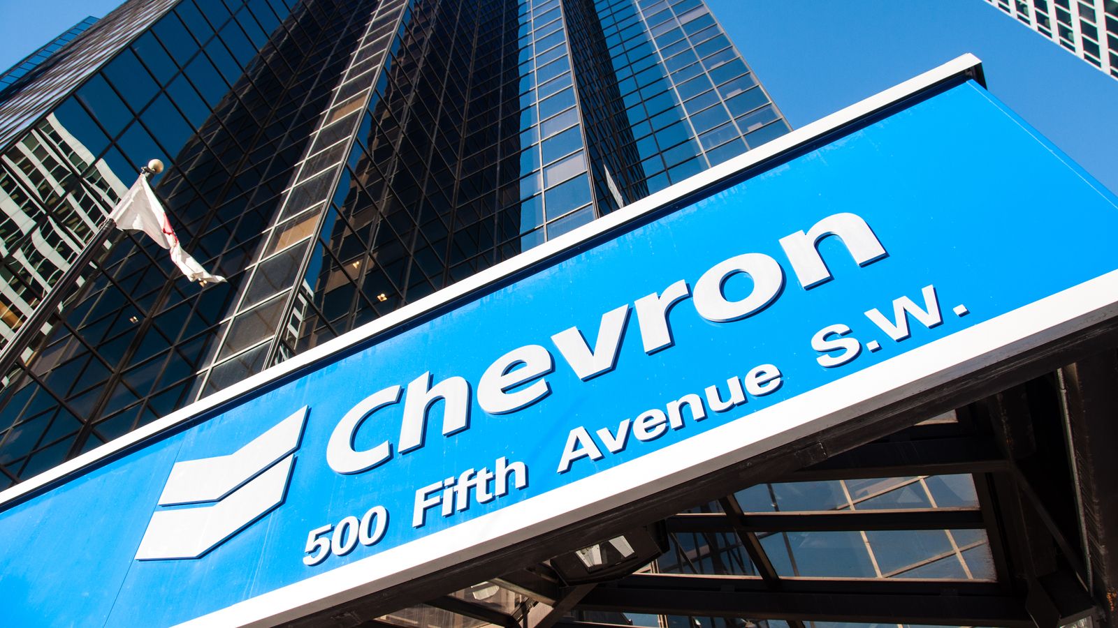 CVX Stock. Chevron logo on blue sign in front of skyscraper building