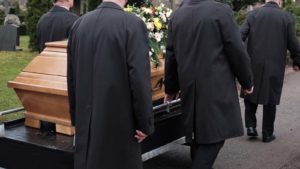 people in suits carry a casket at a funeral