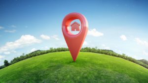 Virtual map pin with house icon on it pinned onto green grass with a blue sky background