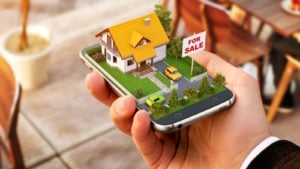 An illustration of a miniature house with a "for sale" sign popping out of a smartphone.
