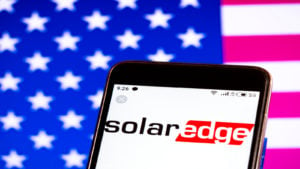 SolarEdge logo on phone with American flag background. SEDG stock. Stock Price Predictions