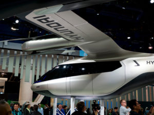 A photo of a flying car prototype on display above roaming people