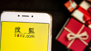 An image of the Sohu.com (SOHU) logo displayed on a phone in front of a background with gifts