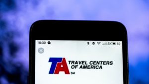 An image of a phone displaying the Travel Centers of America LLC (TA) logo in front of a purple background