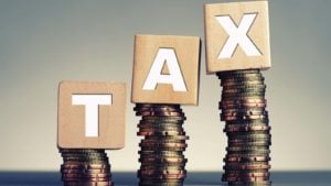 Stacks of coins hold up wooden blocks that spell out "TAX."