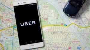 The Uber (UBER stock) logo is displayed on a smartphone on top of a map background.