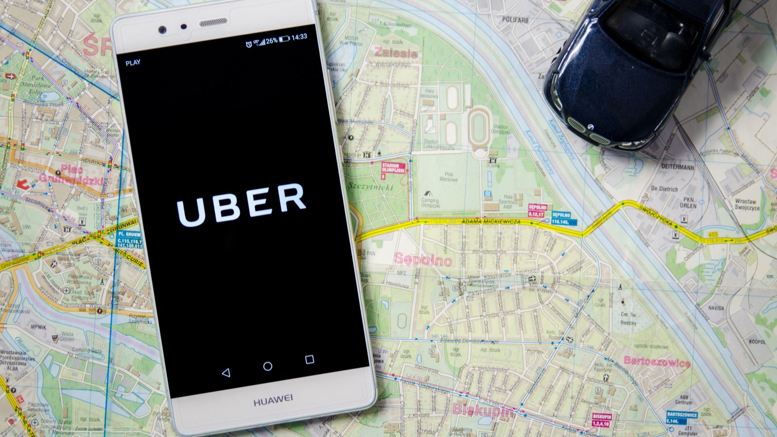 The Uber logo is displayed on a smartphone on top of a map background.