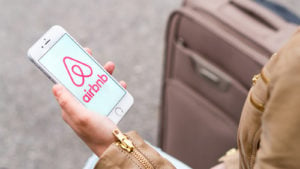 ABNB stock Woman holding mobile phone with the Airbnb logo on the screen