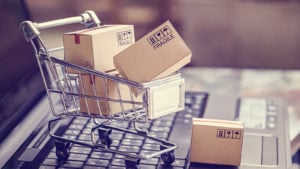 A miniature shopping cart is filled with cardboard boxes. e-commerce stocks