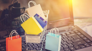 Miniature bags in a shopping cart sit on top of a laptop keyboard. e-commerce stocks to buy