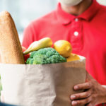 a delivery man in a red shirt dropping off a bag of groceries to represent food and beverage stocks