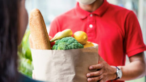 dostavljalec v rdeči srajci, ki oddaja vrečko z živili, ki predstavlja zaloge hrane in pijače
