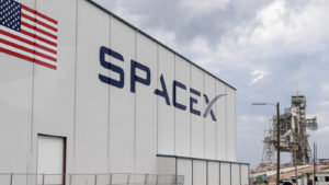 A photo of the SpaceX logo on the side of the building with the American Flag.