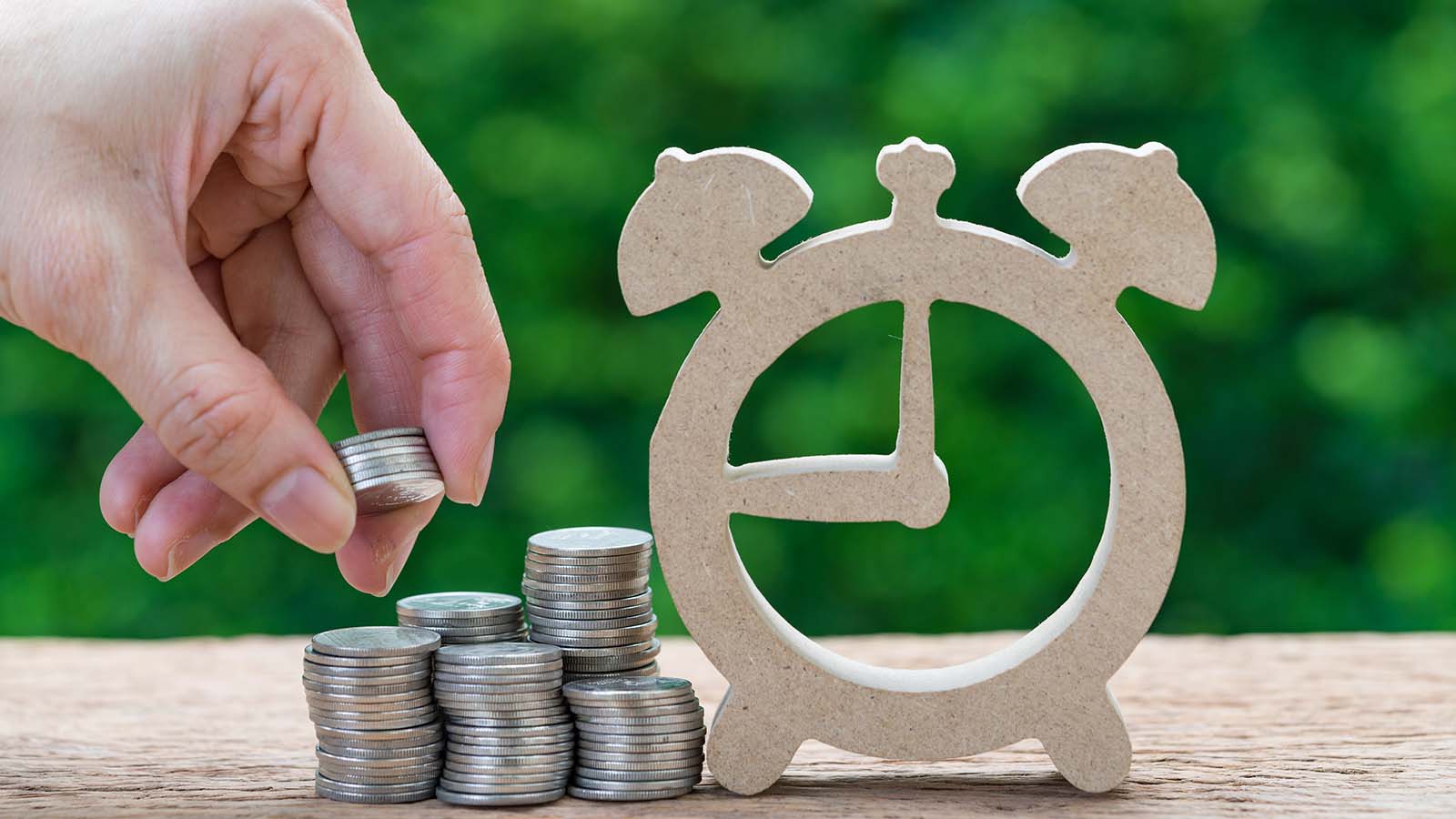 A close-up shot of a hand stacking coins near the outline of a clock. represents long-term stocks to investing for the next decade