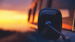 A closeup image of a car's side mirror with a sunset in the background