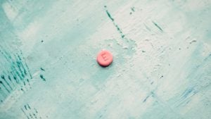 An image of a pink circular pill marked with an "E" displayed on a rigid mint green surface