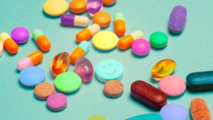 A handful of brightly colored pills in different shapes and sizes is scattered on a turquoise background.