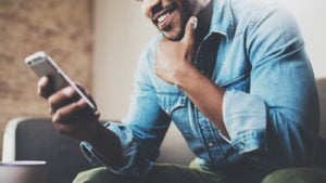 A man sits on his couch looking at his smartphone representing DATS stock.