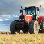 red tractor in yellow field with clouds behind it