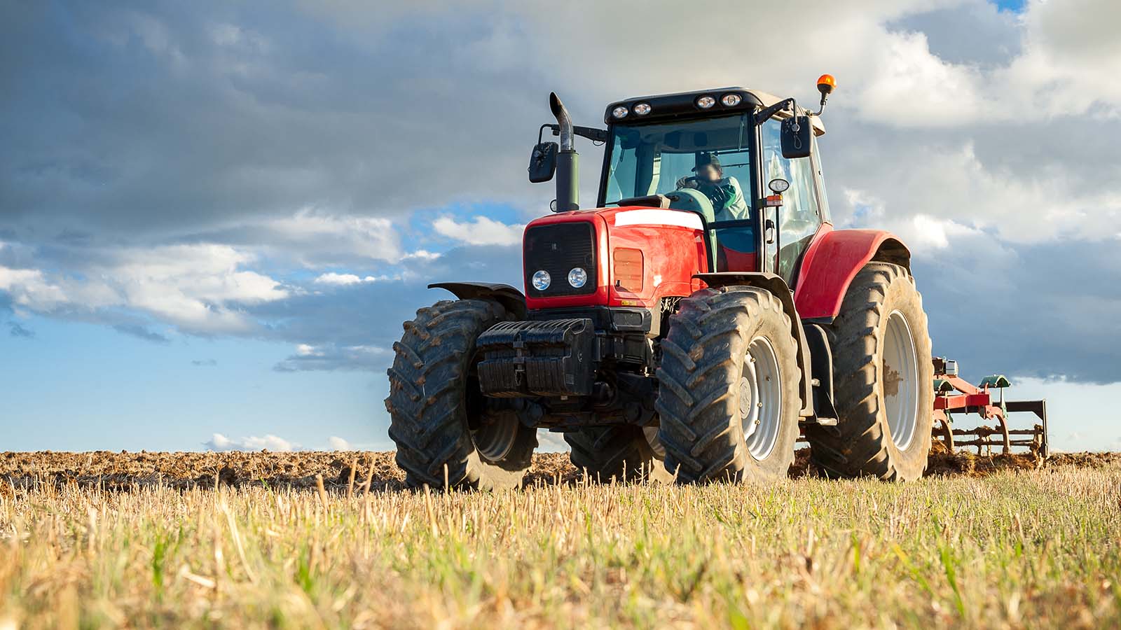 red tractor in yellow field with clouds behind it