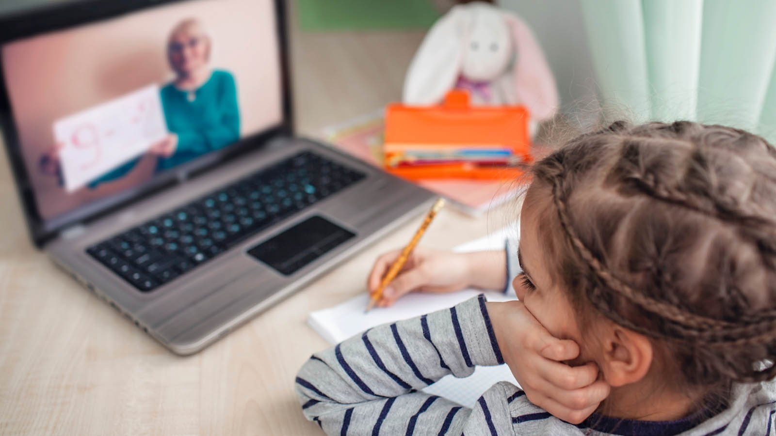 Stock GNS : un enfant devant un ordinateur portable prenant des notes tout en regardant un cours en ligne