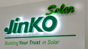 The JinkoSolar (JKS) stock logo displayed on a plain white wall.